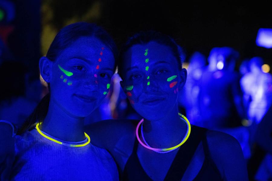 Zwei lächelnde Personen mit fluoreszierender Farbe in festlicher, lebendiger Atmosphäre.