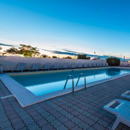 Outdoor pool with sun loungers at sunset.