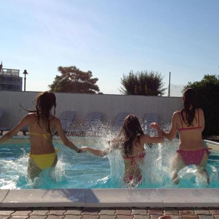 Tre ragazze saltano in piscina al tramonto.