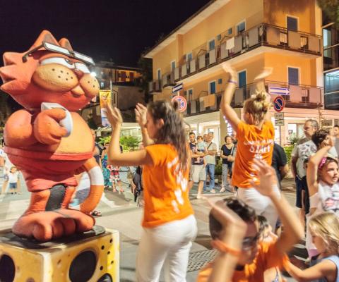 Festa di strada con balli e una mascotte gigante.