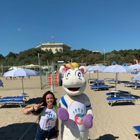 Ragazza felice con mascotte sulla spiaggia soleggiata, ombrelloni e lettini vuoti.