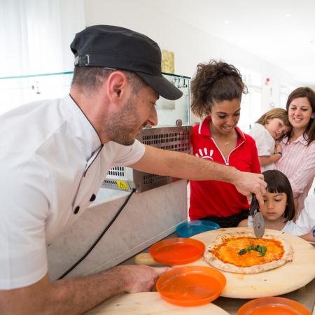 Chef taglia pizza, bambini sorridenti osservano con entusiasmo.