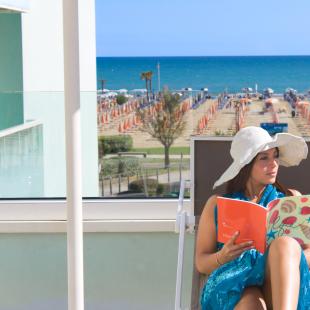 Woman reading on a terrace with sea and beach view.