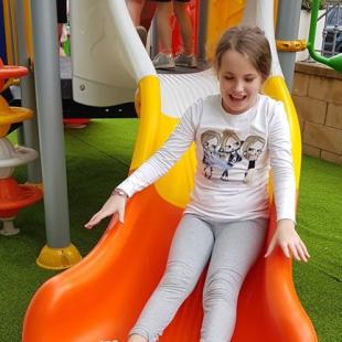 Girl happily slides down an orange slide at the playground.