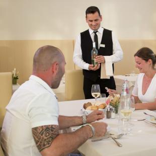 Family dining at restaurant with waiter serving wine.