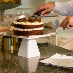 White shirt and vest serving chocolate cake on a white plate.