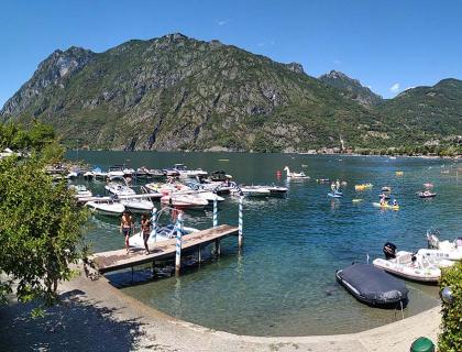 Giornata estiva al lago, barche e nuotatori sotto montagne maestose.