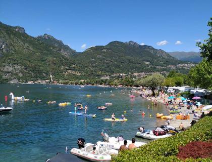 Spiaggia estiva affollata, montagne verdi, cielo azzurro, gioia e relax.