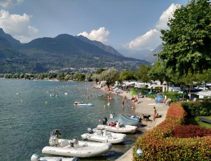 Spiaggia vivace, montagne maestose e barche sul lago in una giornata di sole.