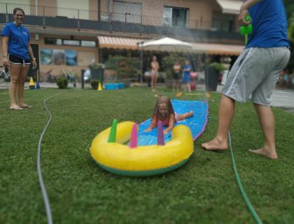 Bambina felice scivola sull'acqua, risate e gioia estiva nel giardino.