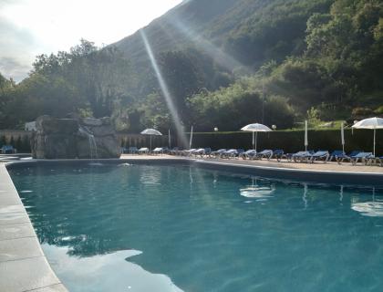 Piscina tranquilla tra montagne, sole e natura rigogliosa.