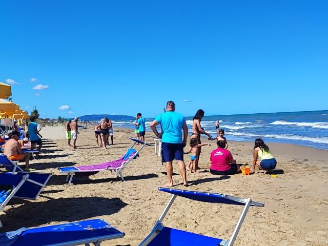 Sunny beach with yellow umbrellas, people relaxing and playing on the sand.