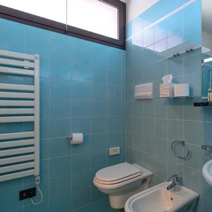 Bagno moderno con piastrelle azzurre, lavabo, WC e bidet.