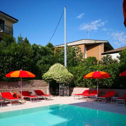 Outdoor pool with red loungers and colorful umbrellas.