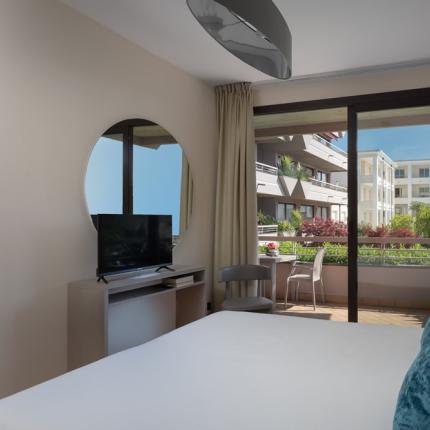 Modern room with balcony, TV, mirror, and view of buildings.