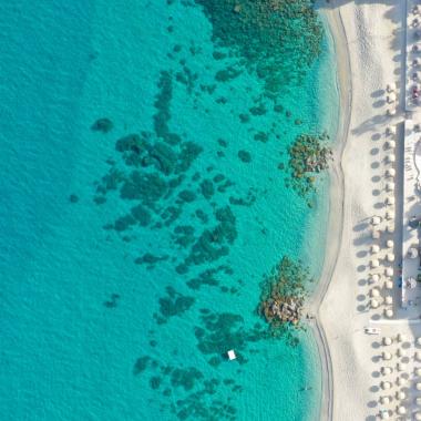 Spiaggia con ombrelloni e piscina vista dall'alto, mare cristallino.