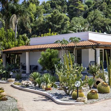 Giardino mediterraneo con cactus e piante grasse, casa bianca con tetto rosso.