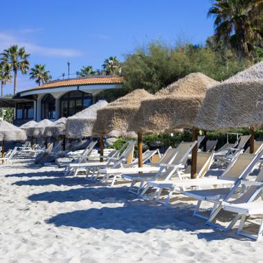 Spiaggia con lettini e ombrelloni di paglia sotto un cielo sereno.