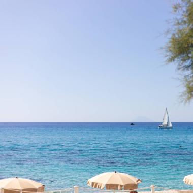 Spiaggia con ombrelloni, barca a vela sul mare azzurro.