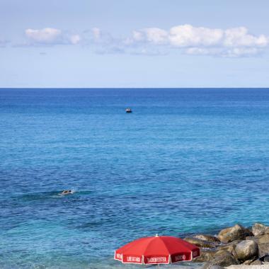 Spiaggia con ombrellone rosso e mare blu, isola in lontananza.