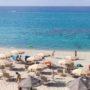 Spiaggia sabbiosa con ombrelloni e mare cristallino, persone che si rilassano.