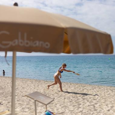 Persone giocano a racchettoni sulla spiaggia sotto un ombrellone.