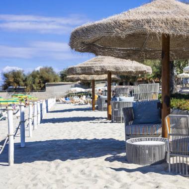 Spiaggia con ombrelloni di paglia e sedie moderne.