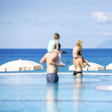 Famiglia in piscina con vista mare e isola in lontananza.