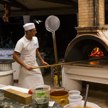 Pizzaioli al lavoro con forno a legna, preparando pizze.