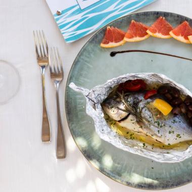 Pesce al cartoccio con agrumi e olive su piatto elegante.