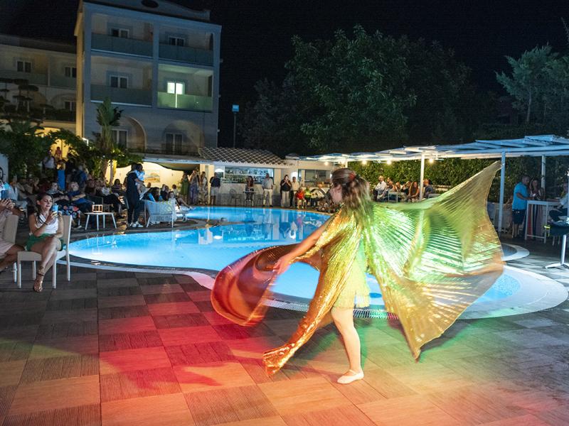 Spettacolo di danza con ali dorate vicino alla piscina di notte.