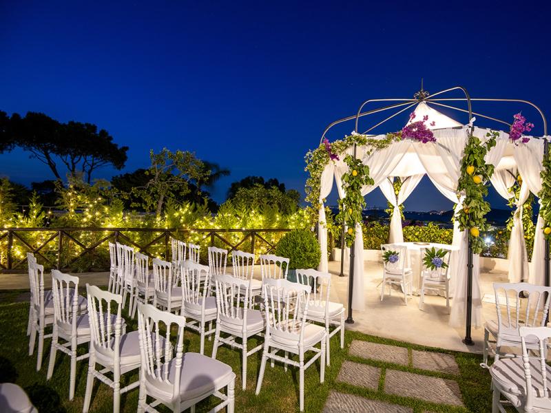 Decorated wedding gazebo with white chairs and lights at night.
