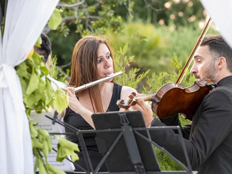 Musical duo plays flute and violin in a garden.