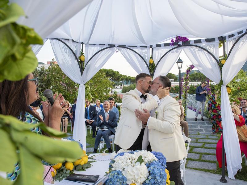 Outdoor wedding ceremony with two grooms kissing.