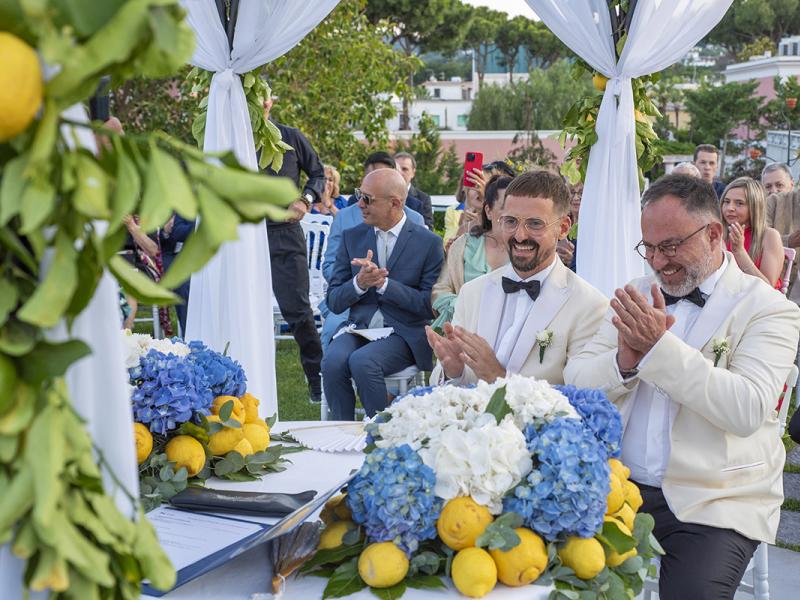 Outdoor wedding with flowers and lemons, happy couple clapping.