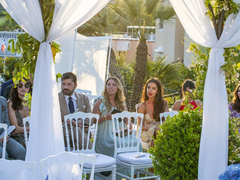 People seated at an outdoor event with floral decorations.