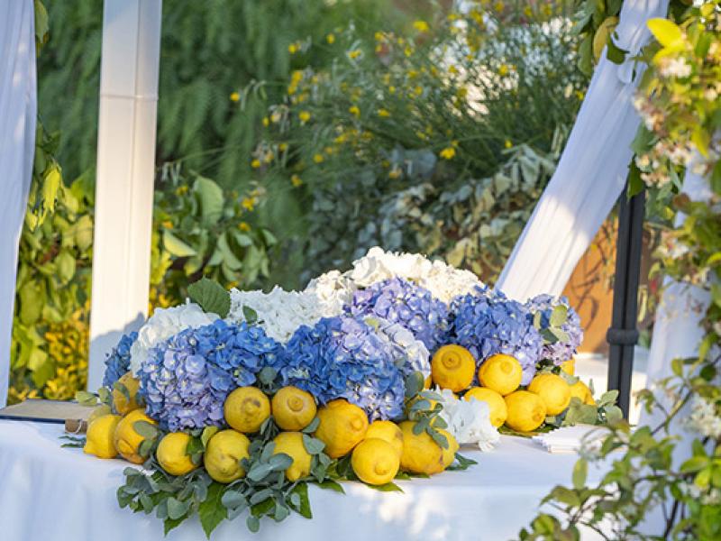 Table decorated with blue hydrangeas, yellow lemons, flowers, and green plants.