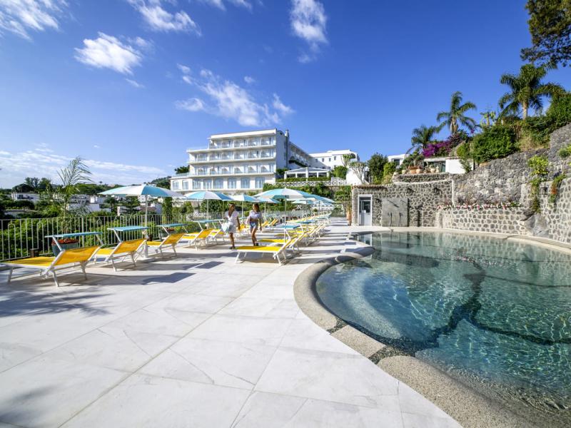 Piscina all'aperto con lettini e ombrelloni in un hotel soleggiato.