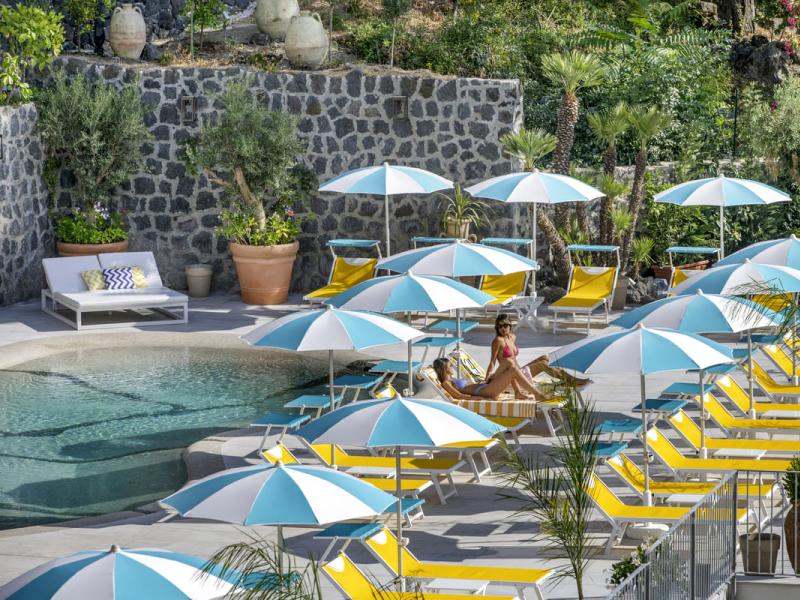 Piscina con lettini gialli e ombrelloni a righe bianche e azzurre.