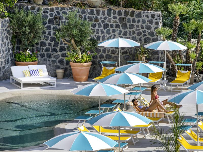 Piscina con lettini gialli e ombrelloni blu e bianchi.