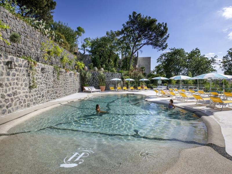 Piscina all'aperto con lettini e ombrelloni, circondata da natura rigogliosa.