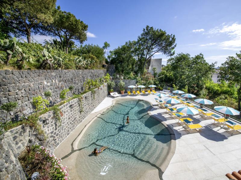 Piscina all'aperto con lettini e ombrelloni, circondata da vegetazione.