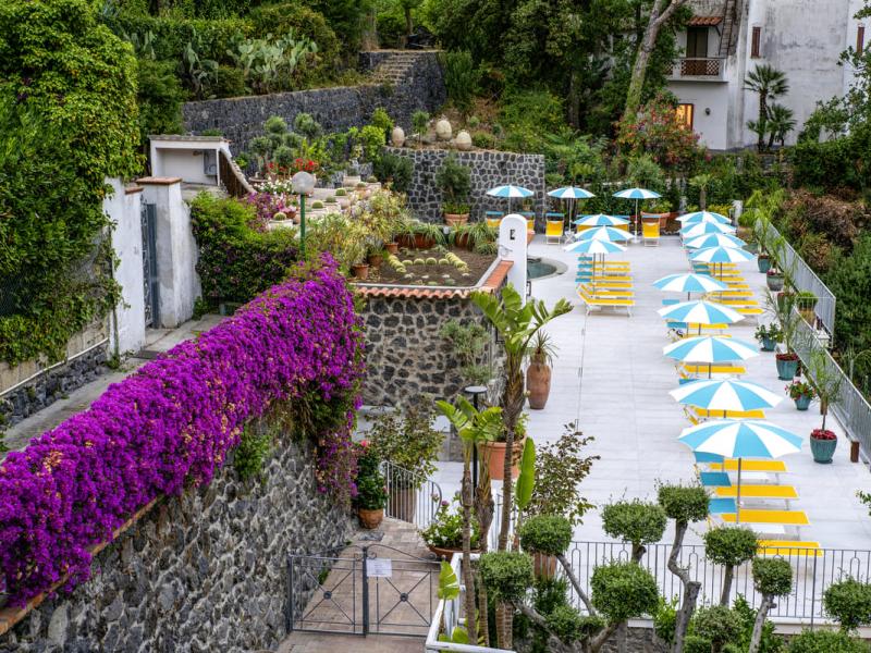 Giardino con sdraio e ombrelloni colorati, circondato da fiori e piante.