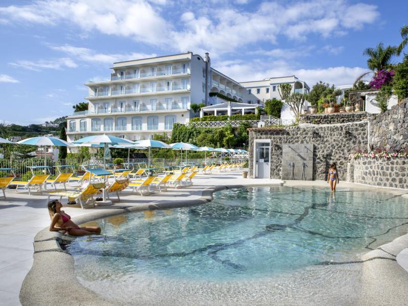 Piscina all'aperto con lettini e ombrelloni, hotel sullo sfondo.