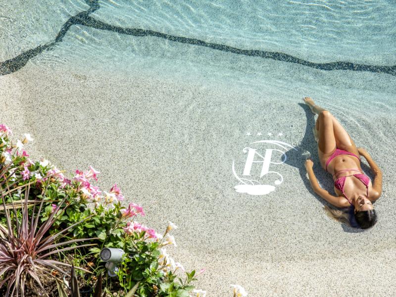 Donna in bikini rosa rilassata in piscina accanto a fiori.
