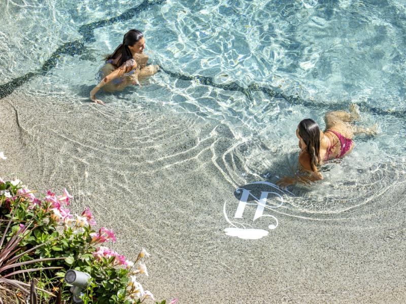 Due donne in piscina con fiori colorati intorno.