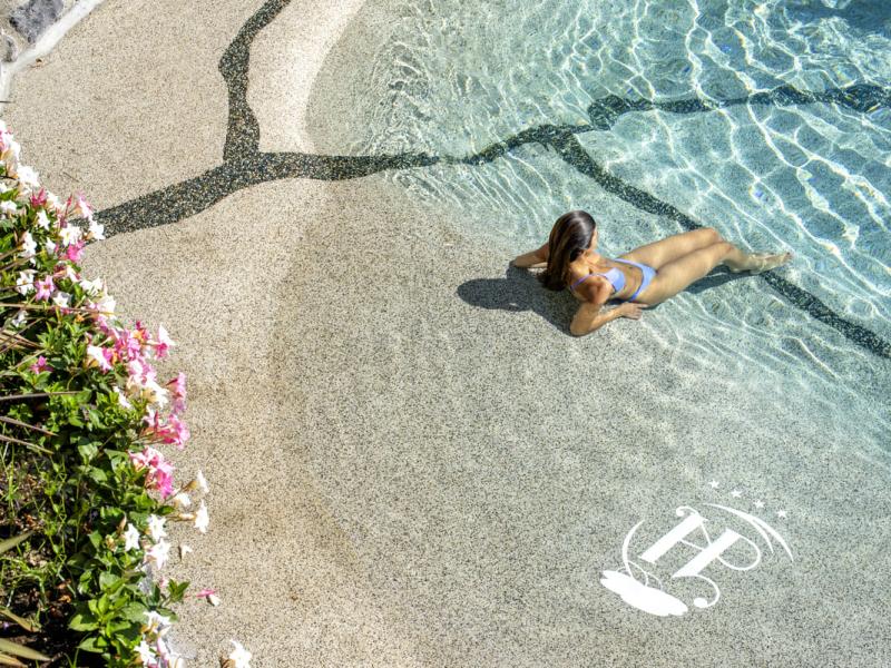 Donna in piscina con fiori e sole.