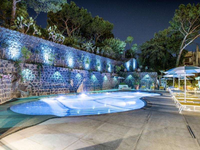 Piscina illuminata di notte con lettini e ombrelloni.