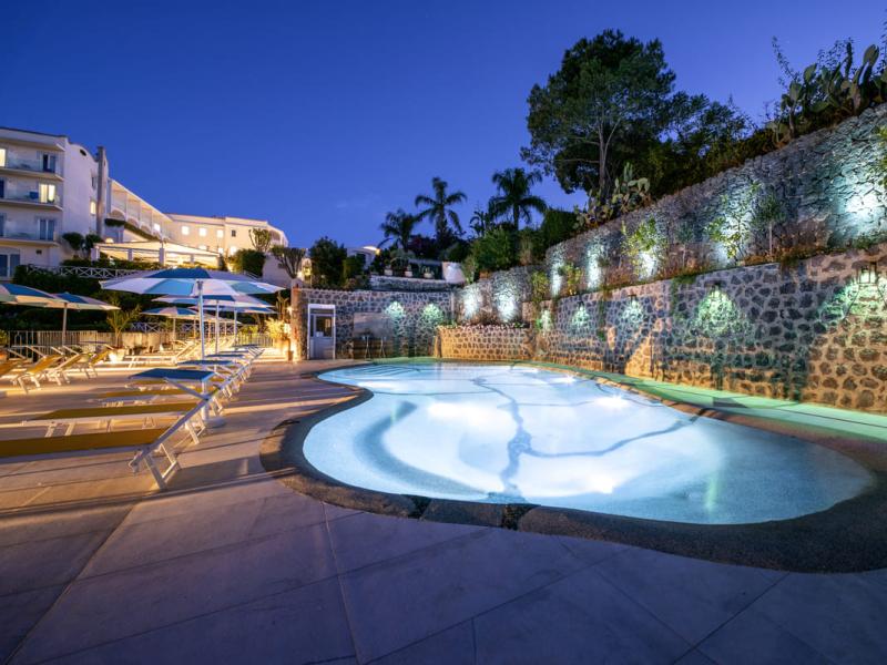 Piscina illuminata di notte con lettini e ombrelloni.