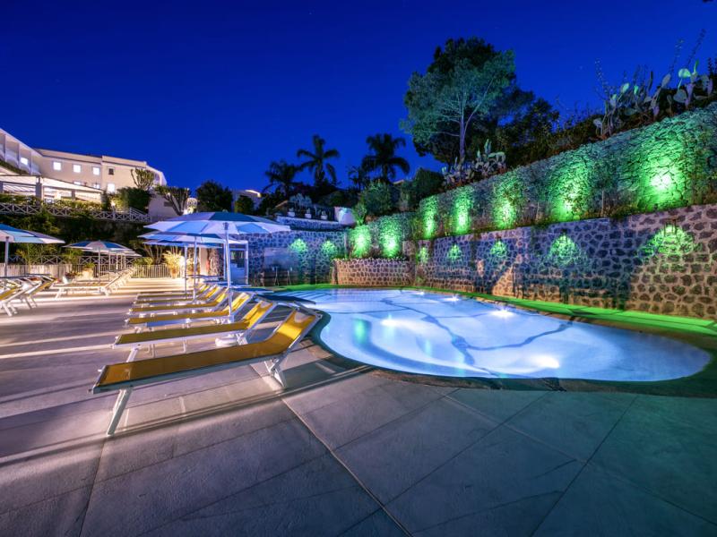 Piscina illuminata di sera con lettini e ombrelloni.